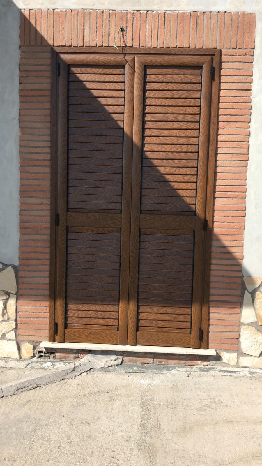 Una porta di legno con persiane su un muro di mattoni.