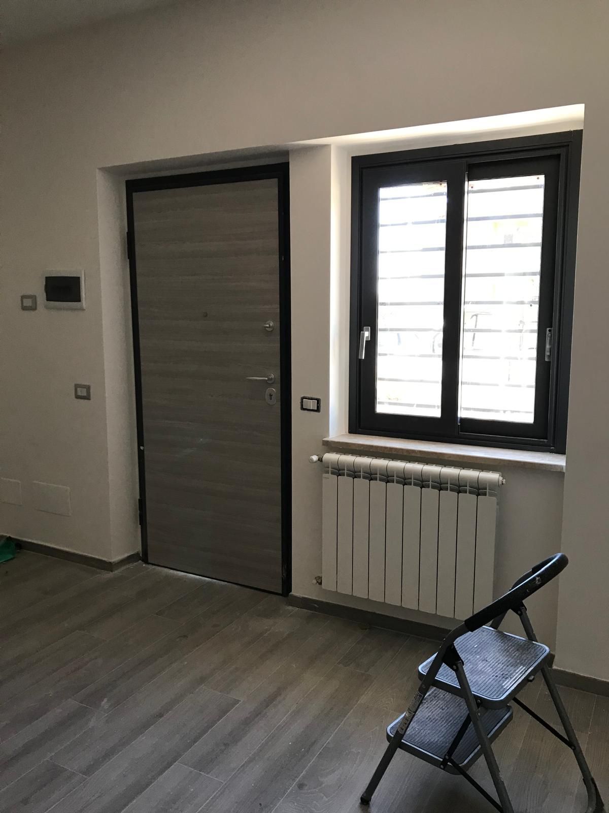 Una stanza con una porta, un termosifone e una finestra.