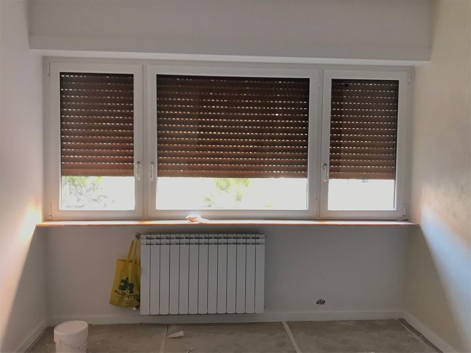 Una stanza vuota con tre finestre e un termosifone