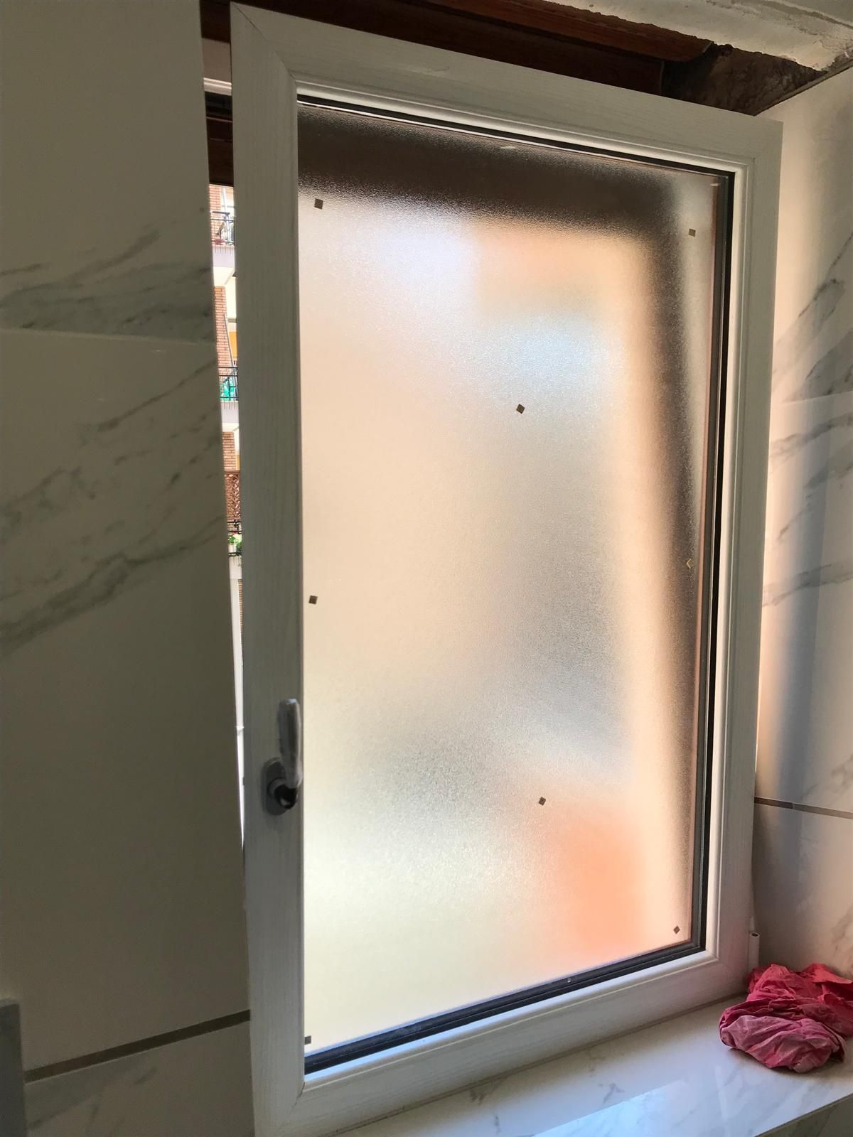 In un bagno è aperta una finestra bianca con vetro smerigliato.