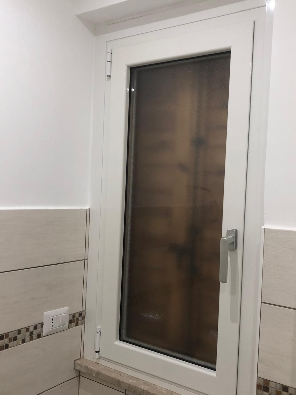 Una finestra bianca con una zanzariera in un bagno.