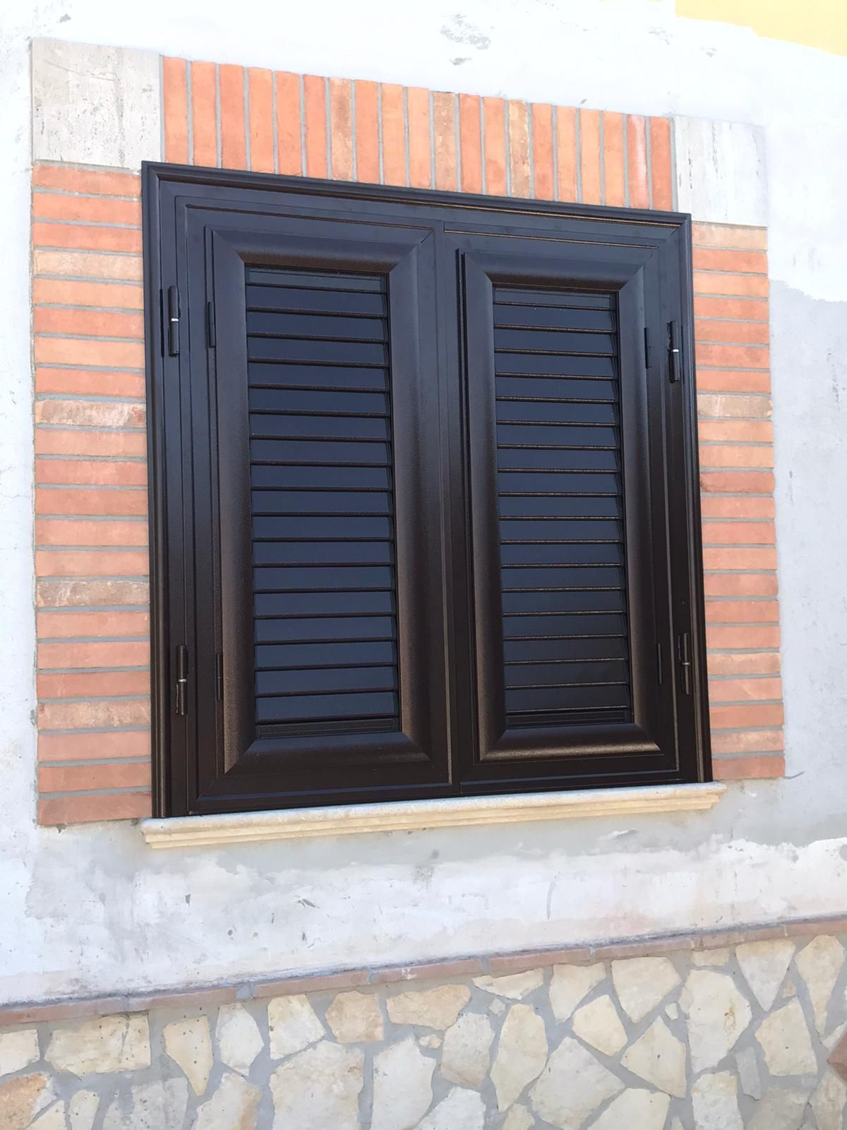 Una finestra con persiane nere su un muro di mattoni