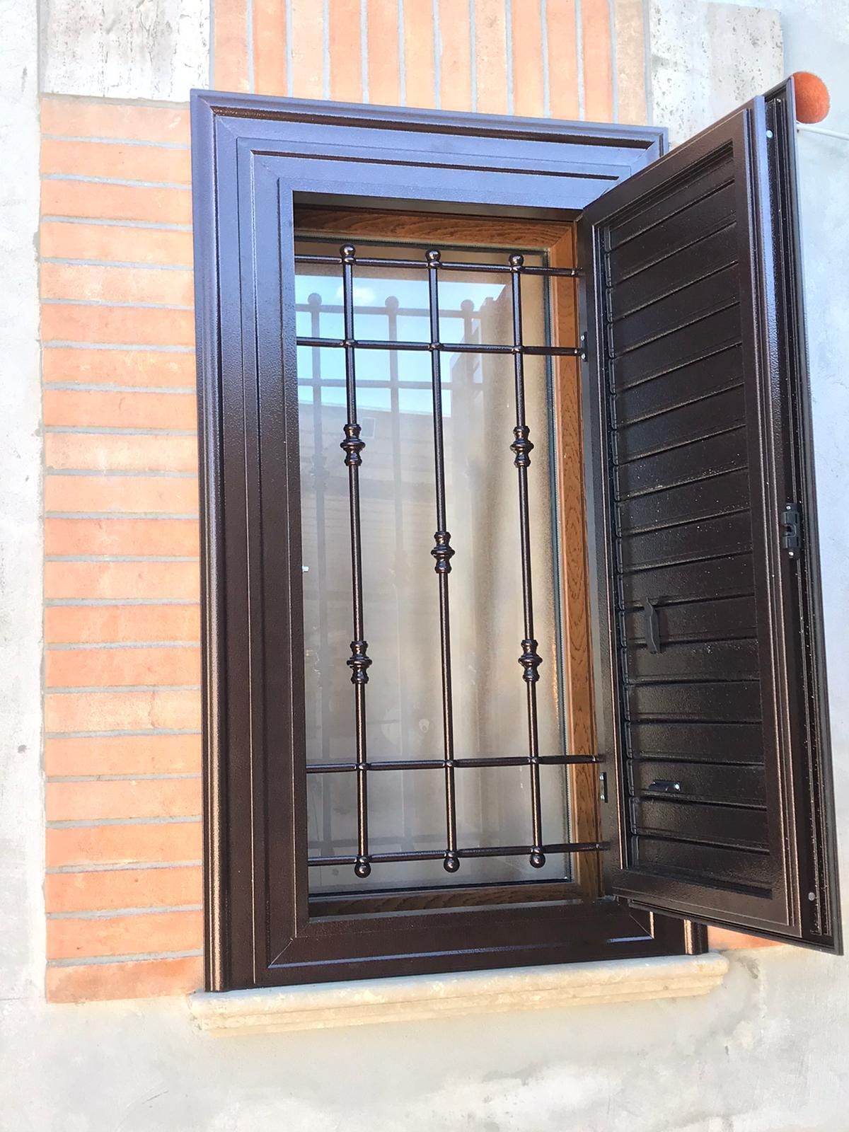 Una finestra con grata in ferro battuto e persiane su un muro di mattoni.