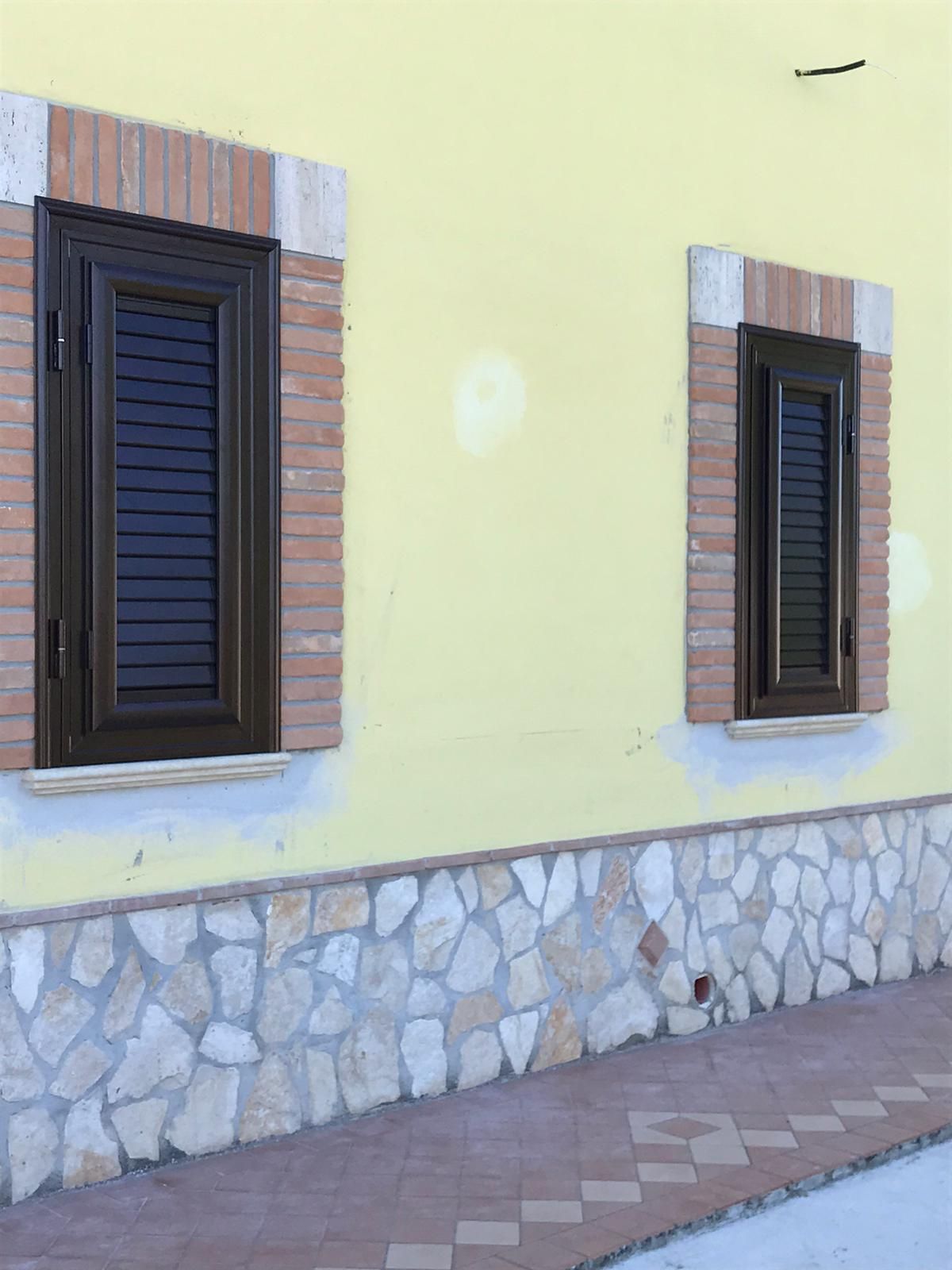 Un edificio giallo con due finestre e un muro di pietra