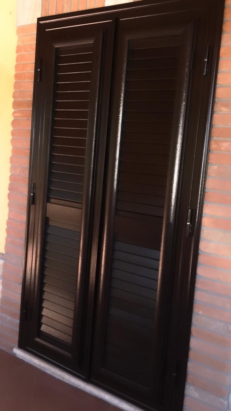 Una porta nera con le persiane è appoggiata a un muro di mattoni.