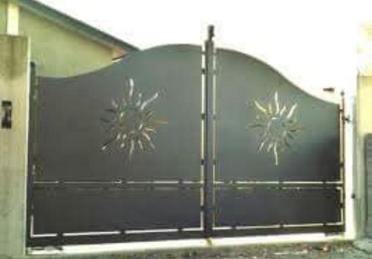 Un cancello nero con un sole sopra si trova di fronte a una casa.