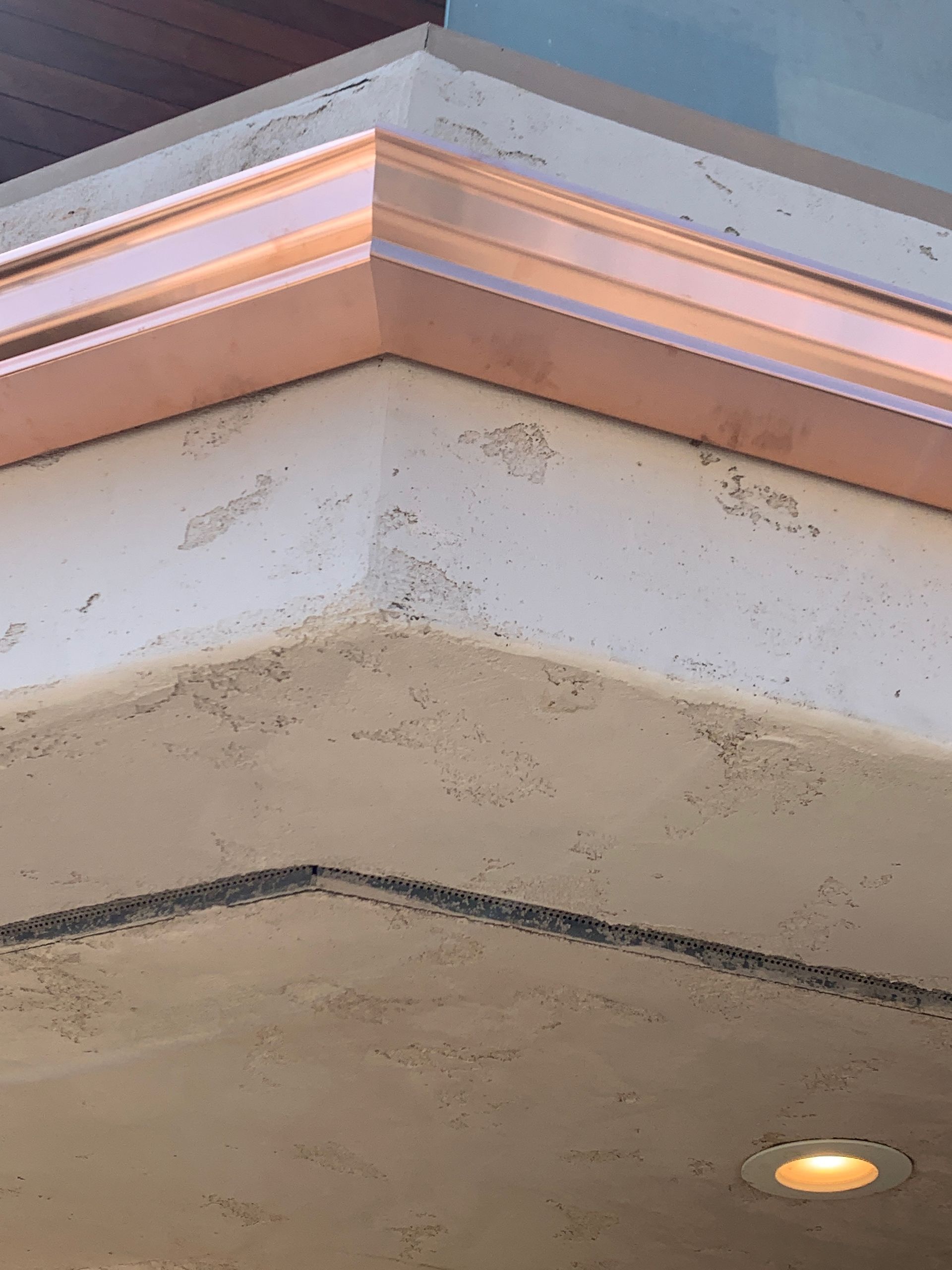 Corner of a building with copper trim on textured tan surface, and recessed lighting.