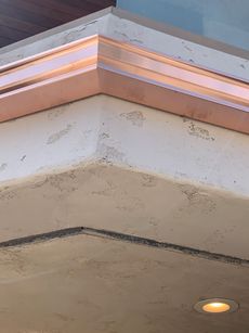 Copper trim on textured light-colored concrete corner. Recessed light at bottom.