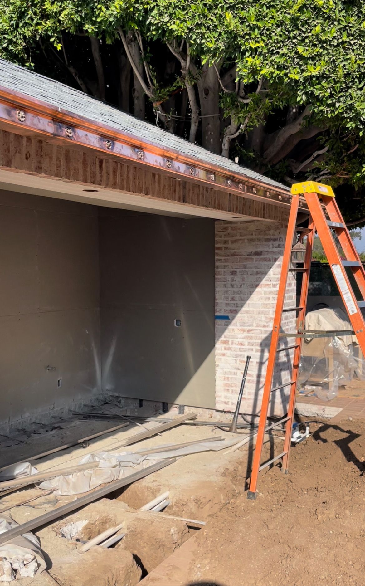 Construction of a building exterior: brick wall, plastered wall, orange ladder, and wooden frame.