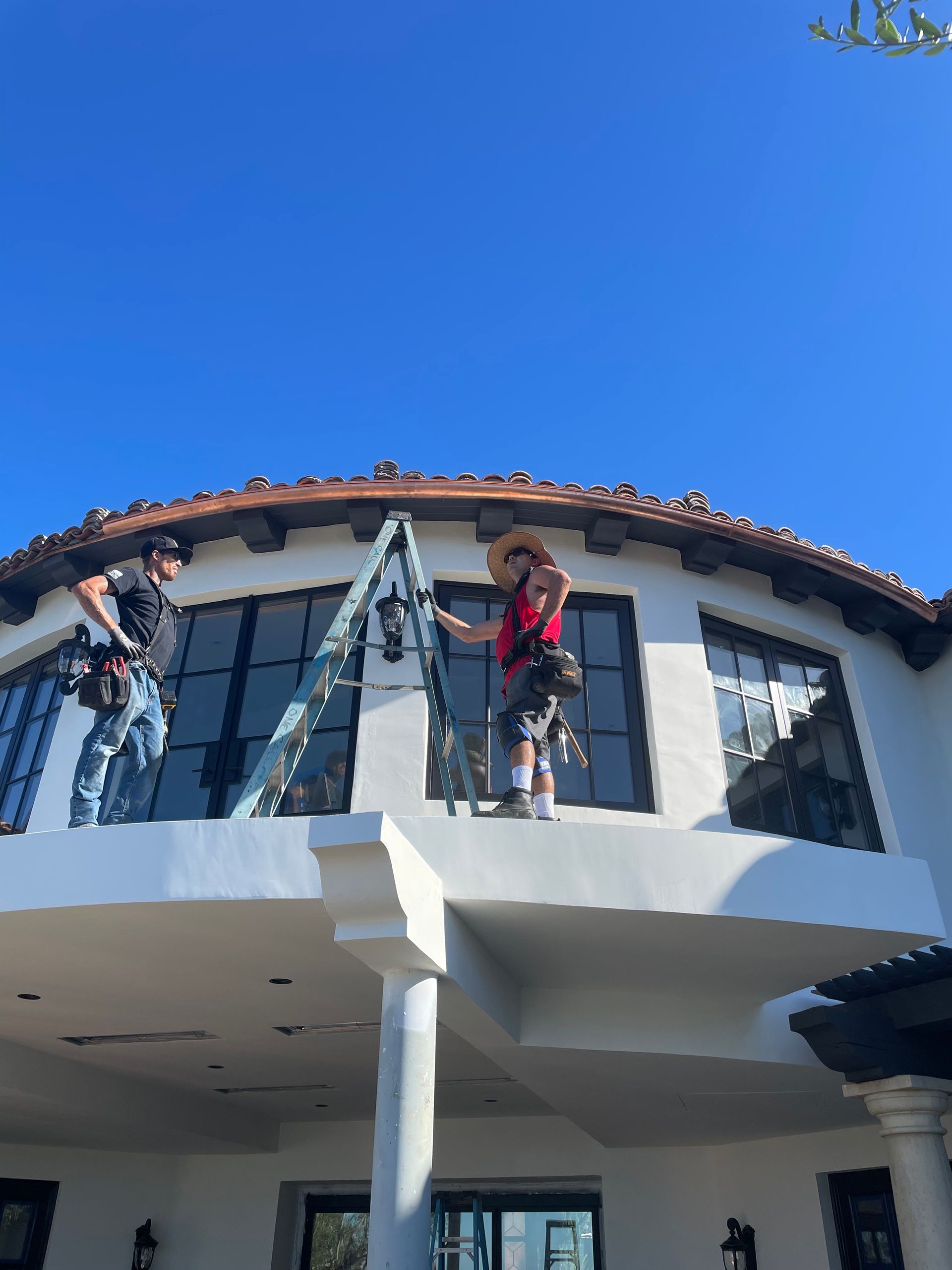 Two men cleaning windows on a white building with arched windows. One is on a ladder, and the other is nearby.