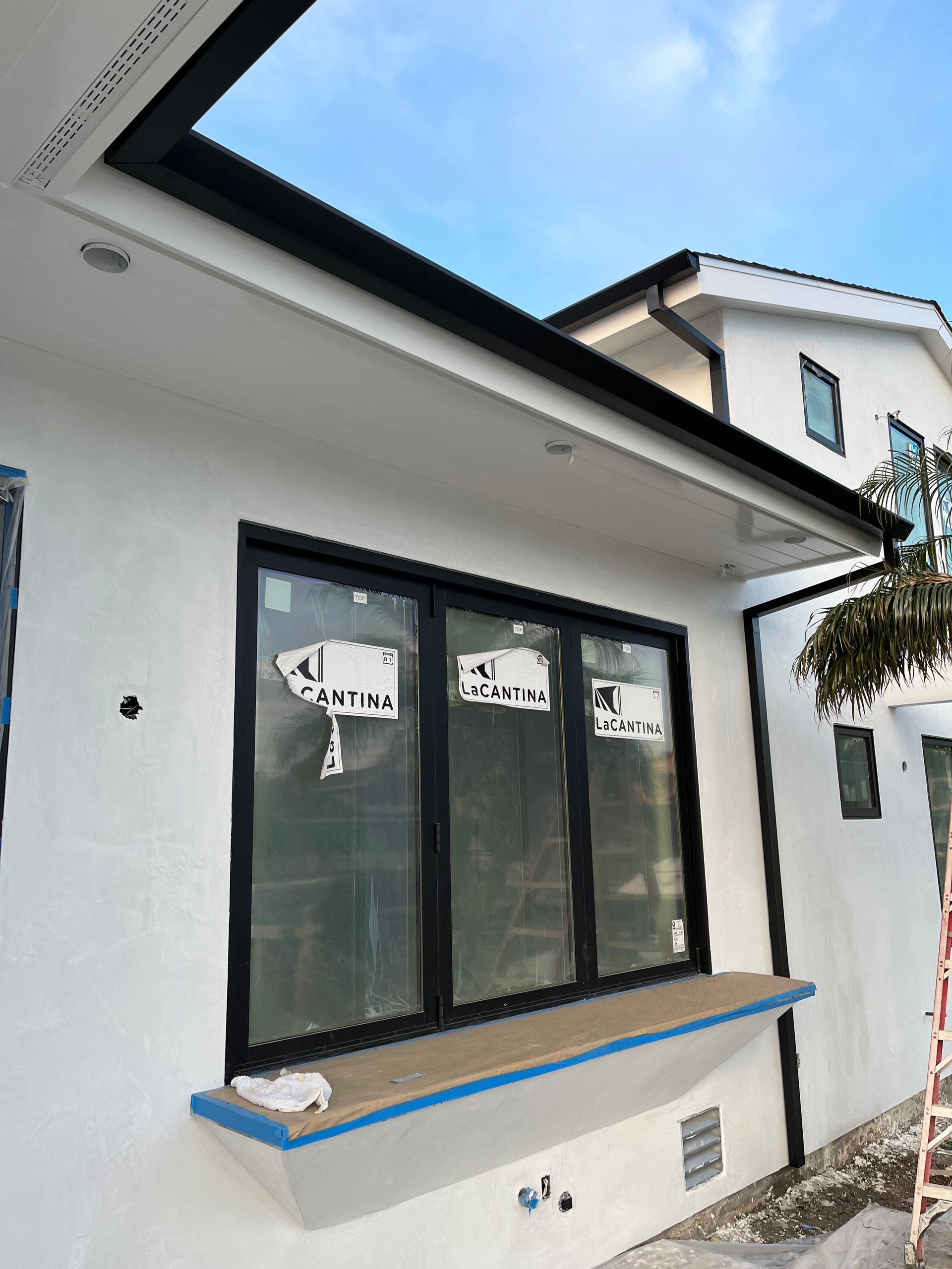 Exterior view of a house with a black-framed window and trim, white walls, and a blue sky.
