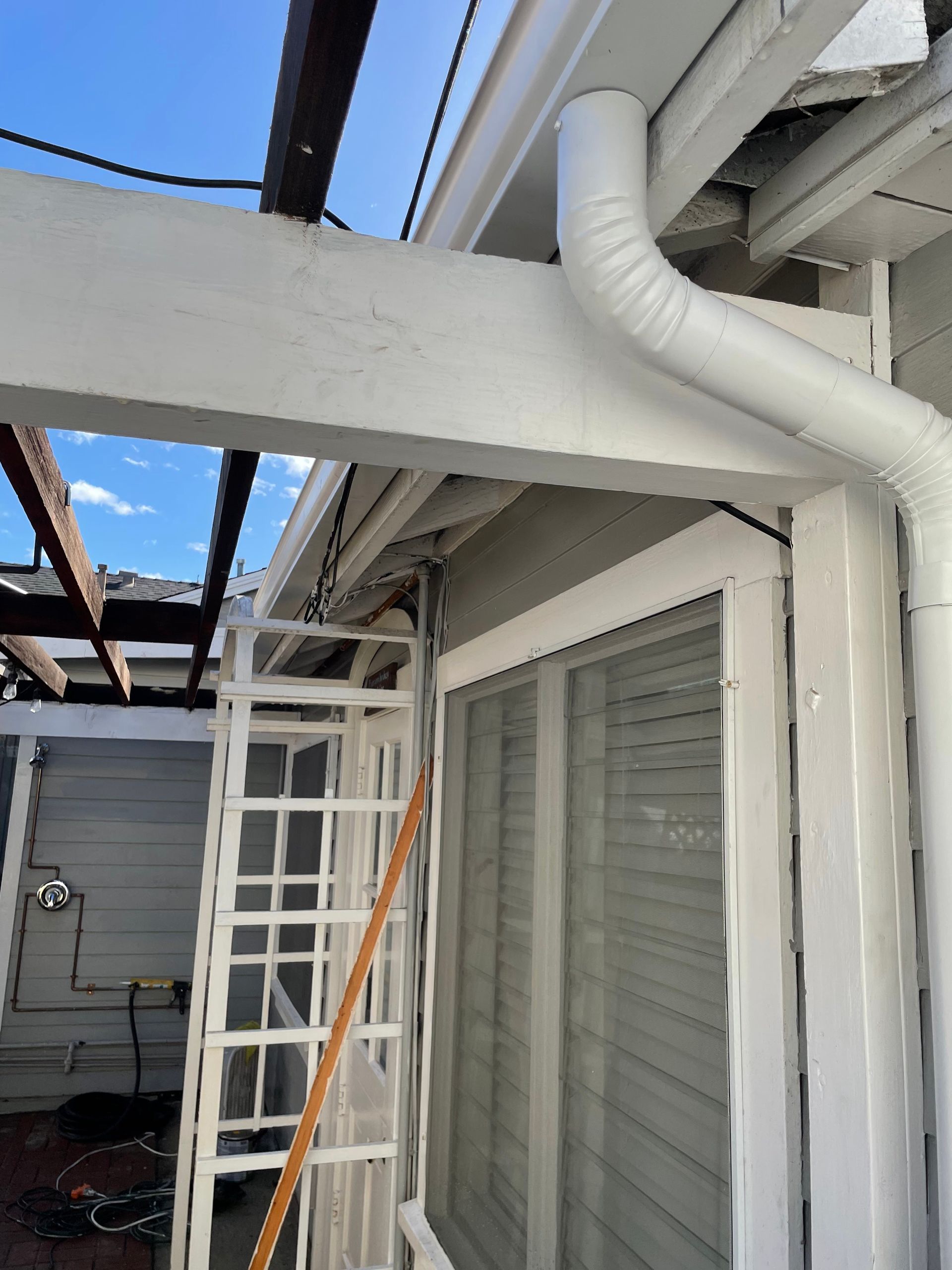 White exterior of a building with a gutter and downspout. A ladder leans against a window.