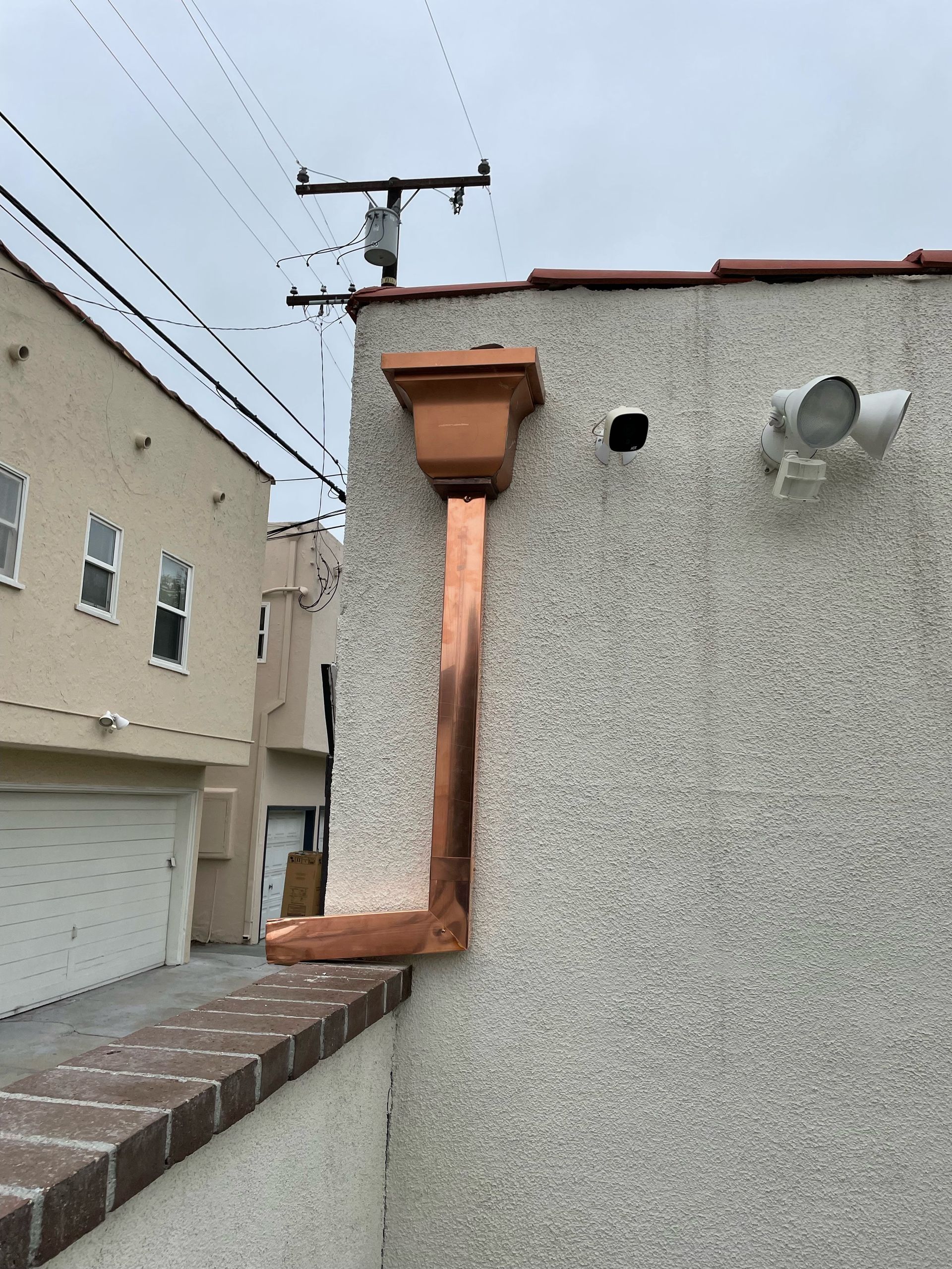 Copper guttering on a stucco building, with a brick wall in the foreground.