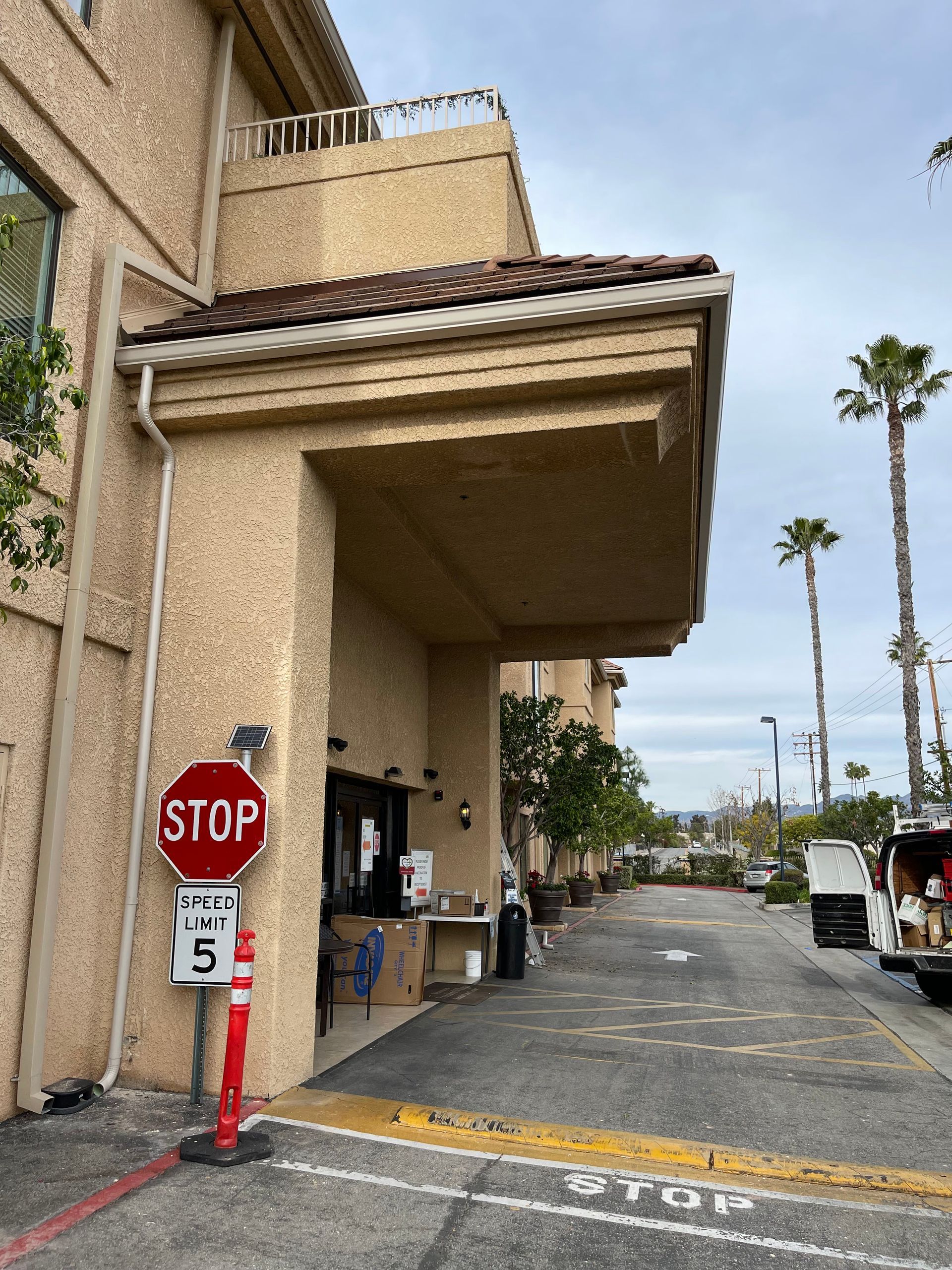 Exterior view of building with drive-up window; stop sign, palm trees, and car on the right.