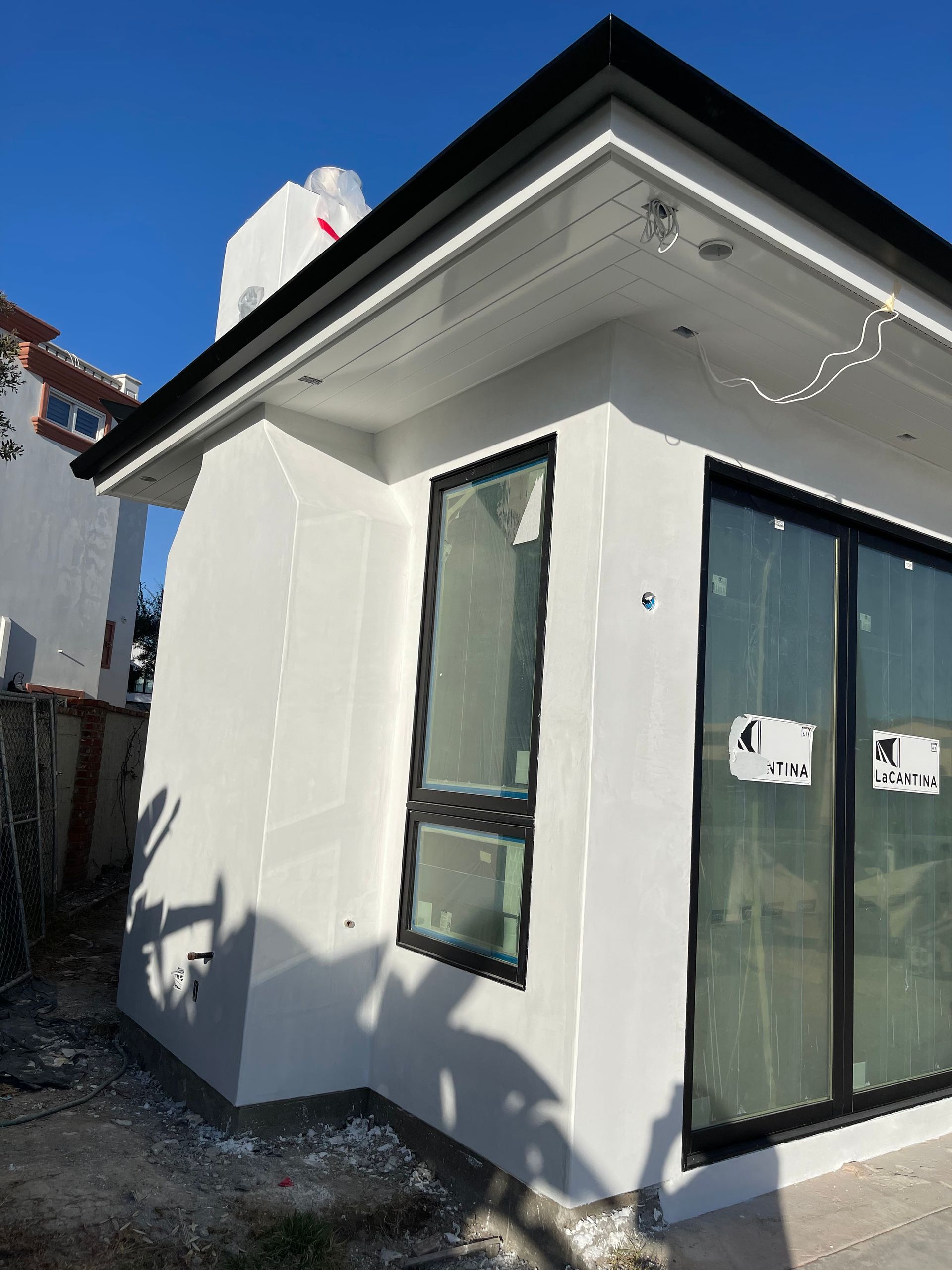 White building with black-framed windows and door under construction, against a blue sky.