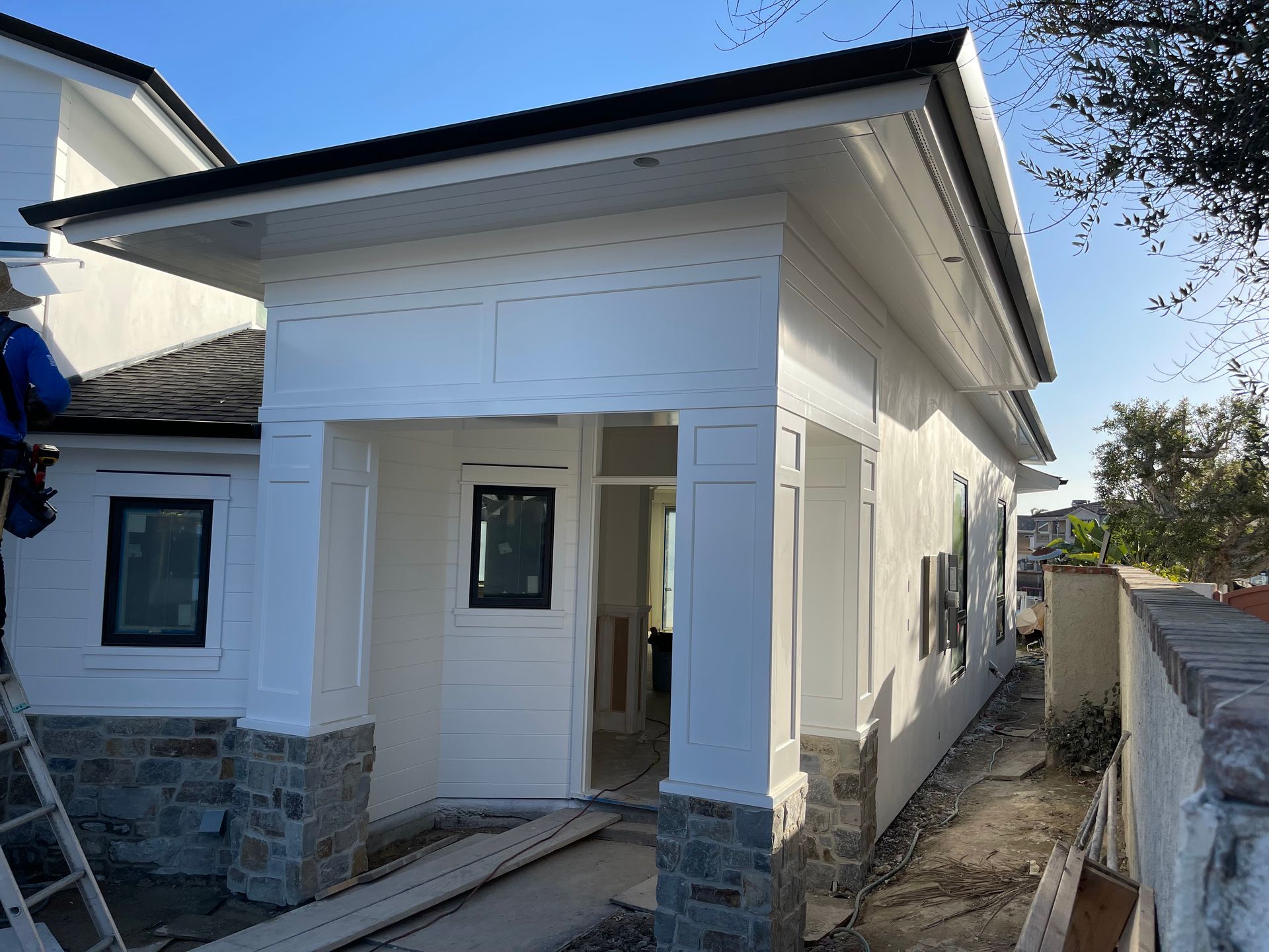 White building with stone accents, black roof, construction materials on the ground.