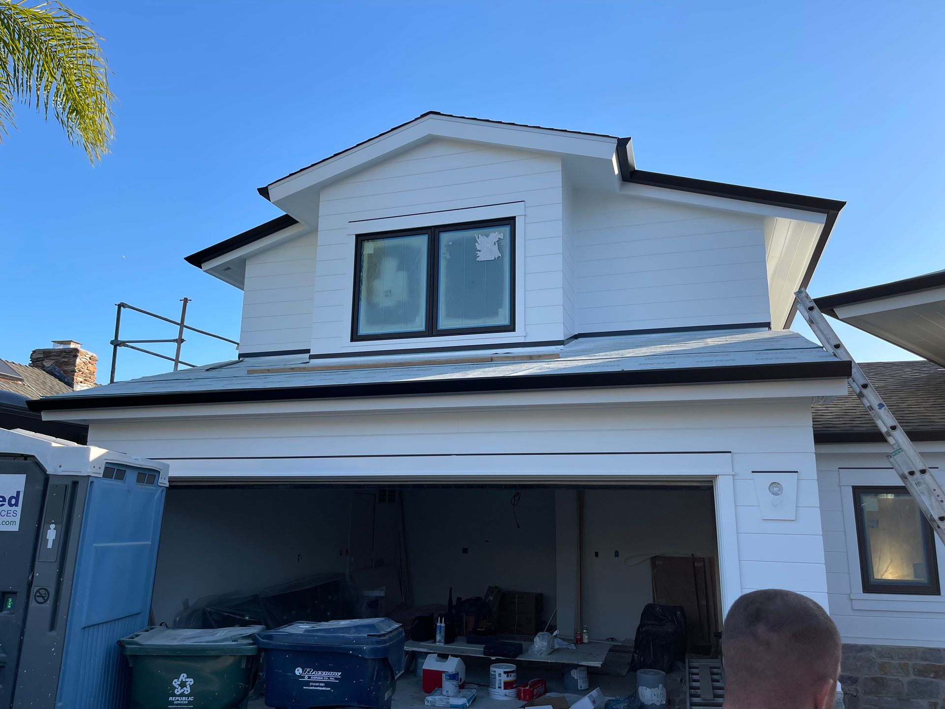 White house under construction, black trim, blue sky, construction tools.