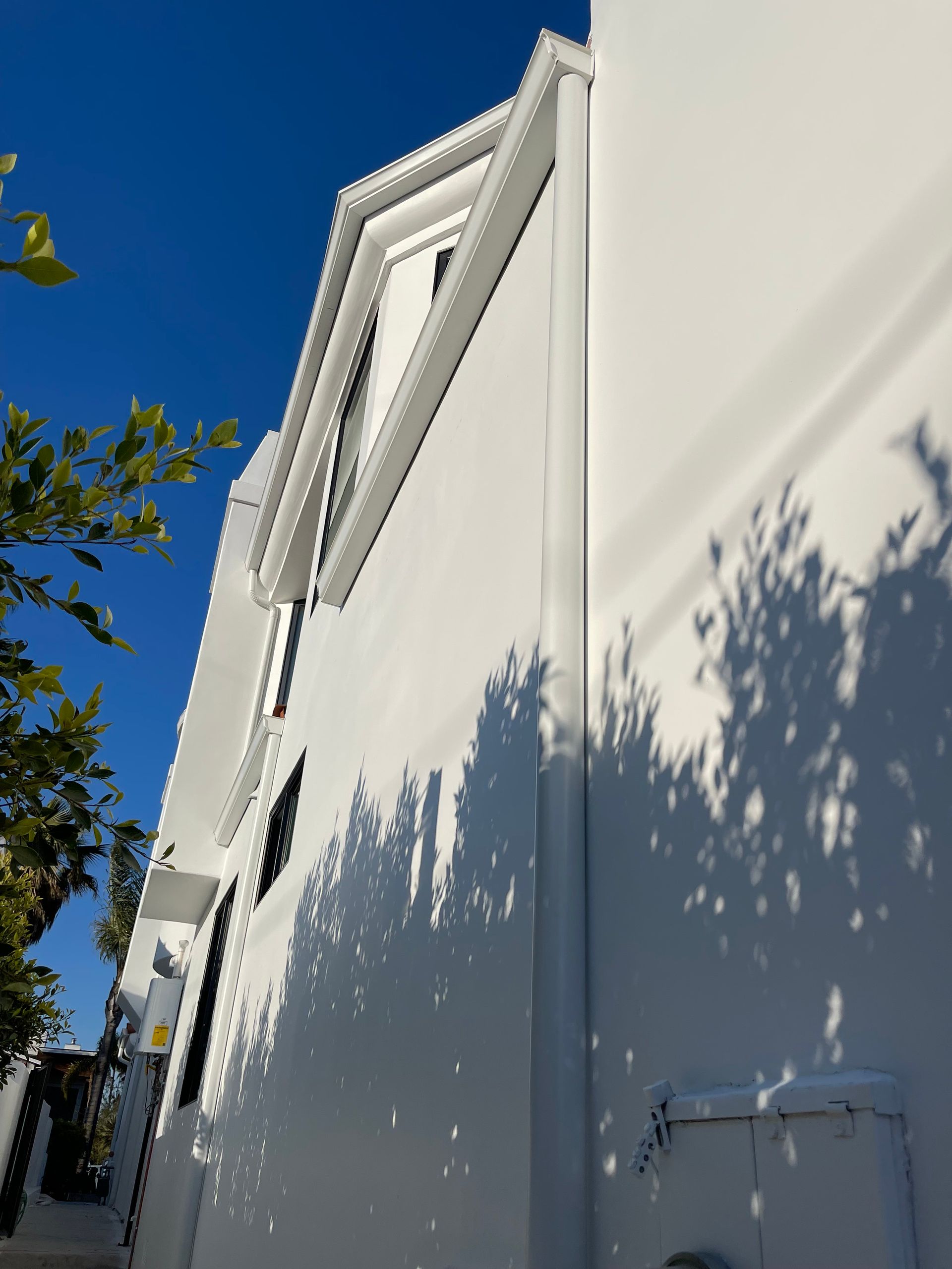 White building exterior with shadows from tree on a bright blue sky day.