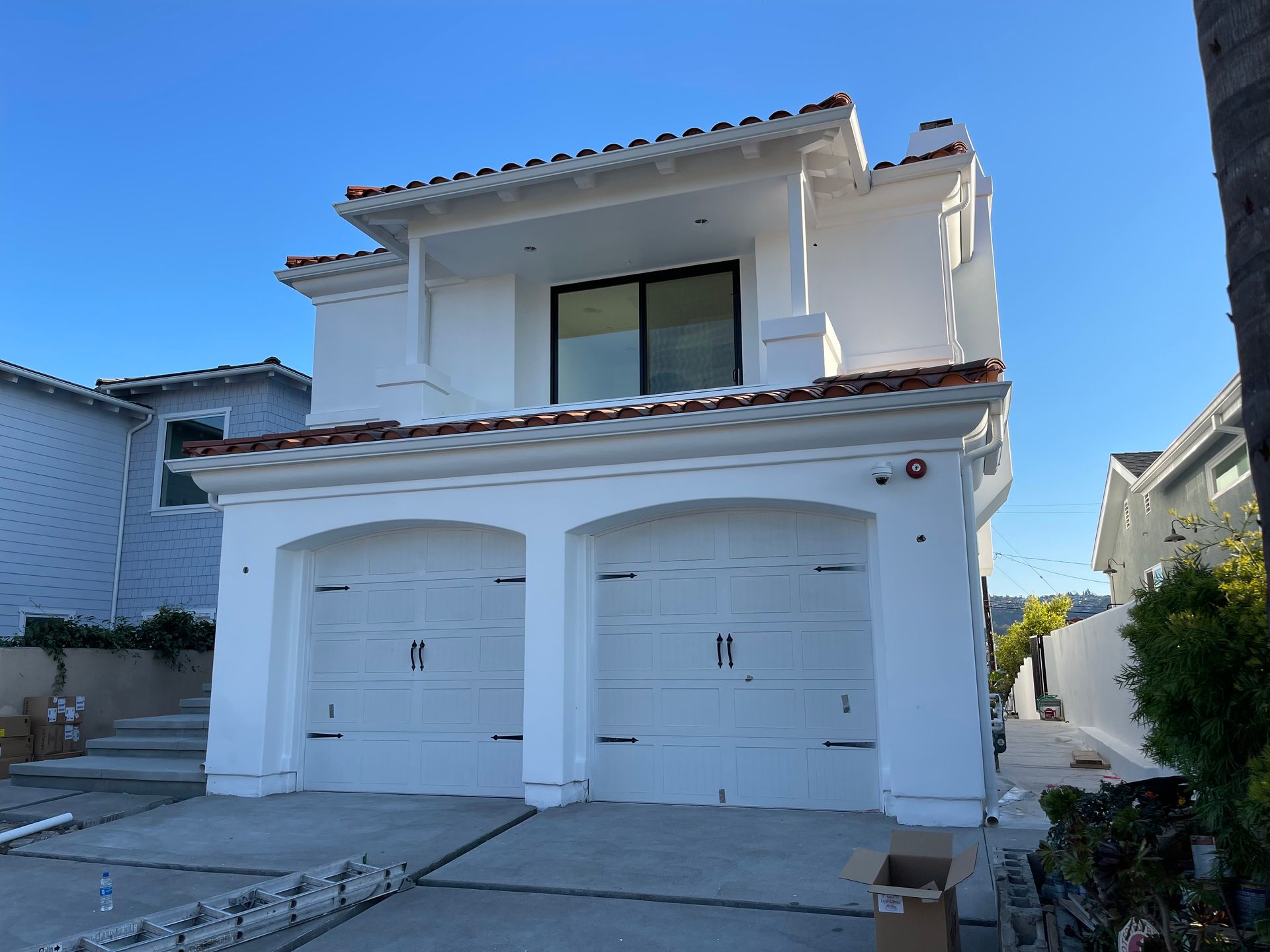 White stucco house with red tile roof, two-car garage, and blue sky.