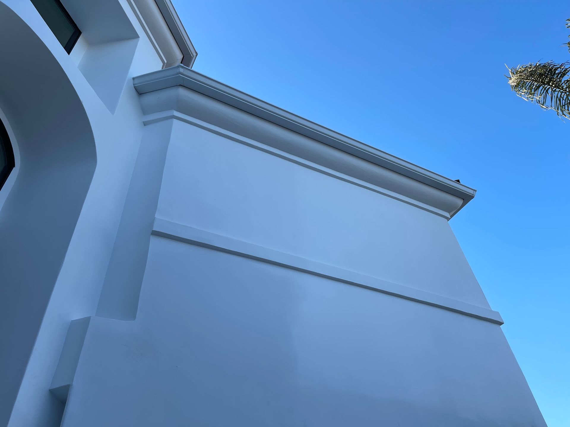 White stucco building with decorative trim against a bright blue sky.