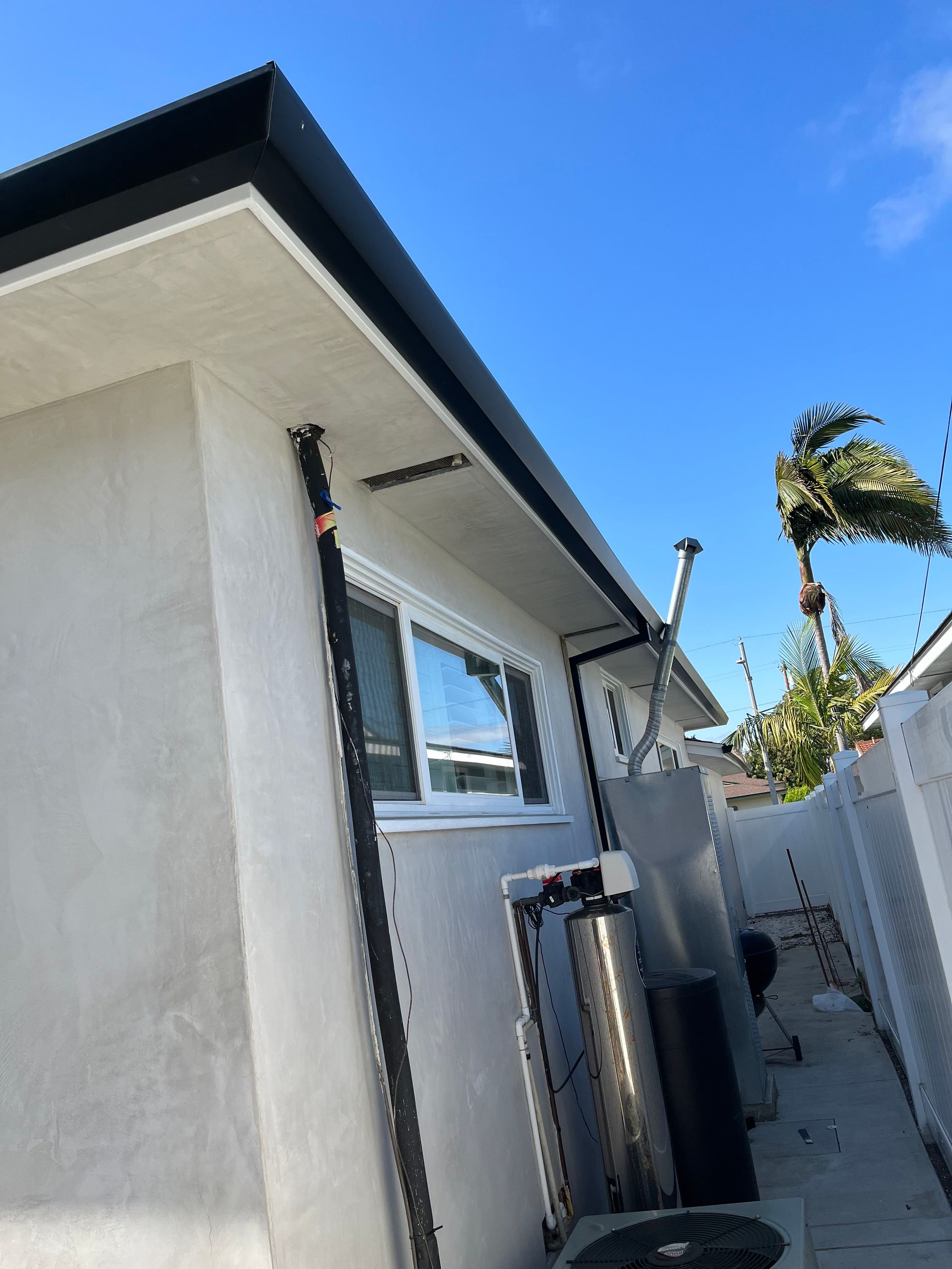 Exterior of a house with black gutters, grey stucco walls, and blue sky.