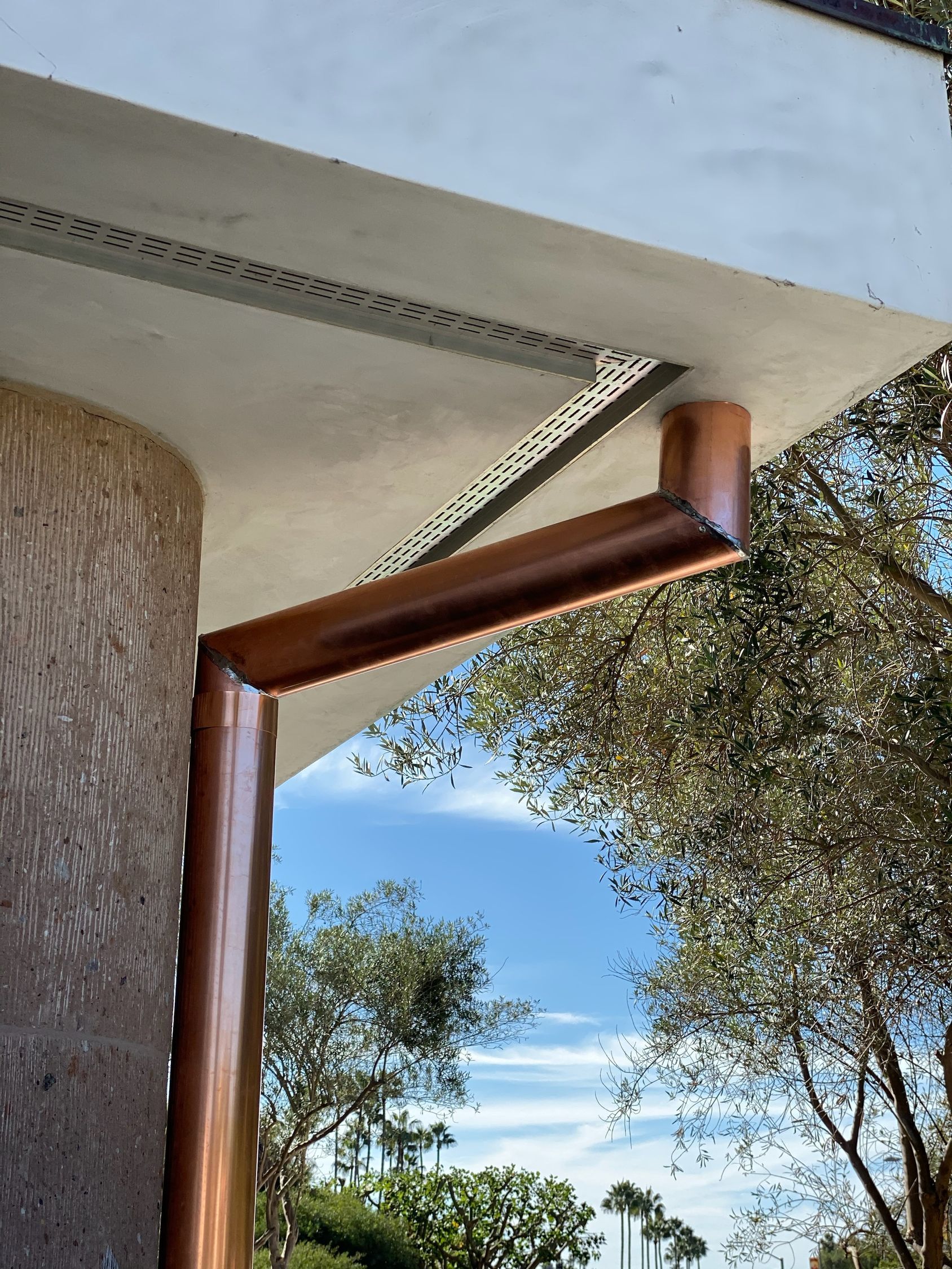 Copper rain gutter on a building corner, with a blue sky background.