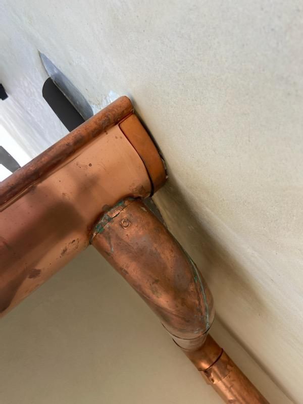 Copper guttering bends at a corner, mounted on a cream wall.