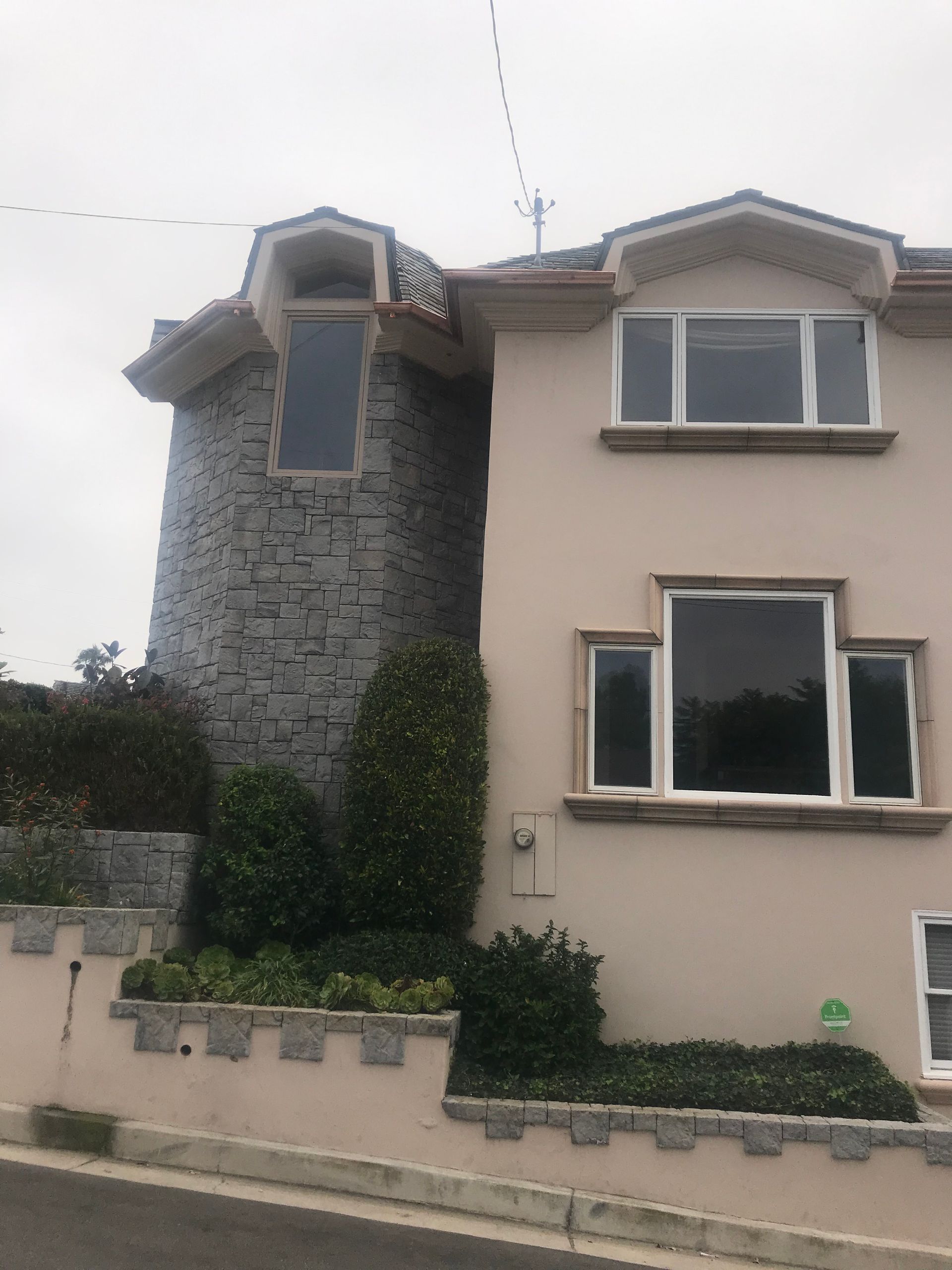 Stone tower next to a light pink building with white window frames. Green shrubs along the base.