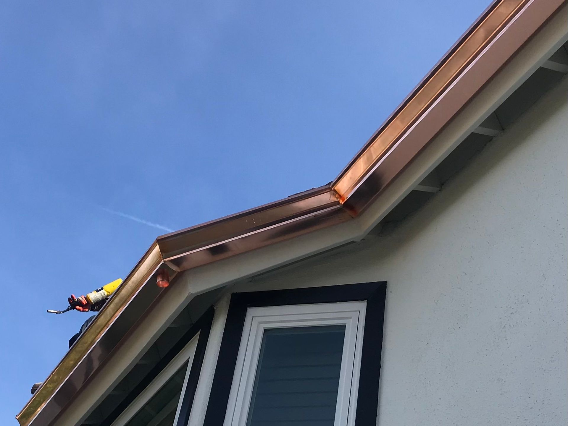 Copper gutters on a white house with a blue sky, a person works on the roof.