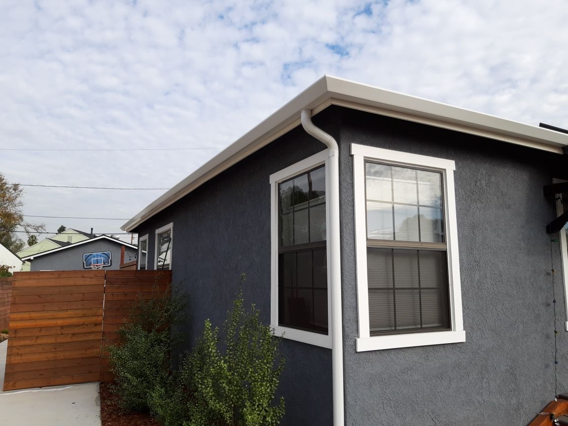 Gray building with white-framed windows and a matching gutter under a cloudy sky.