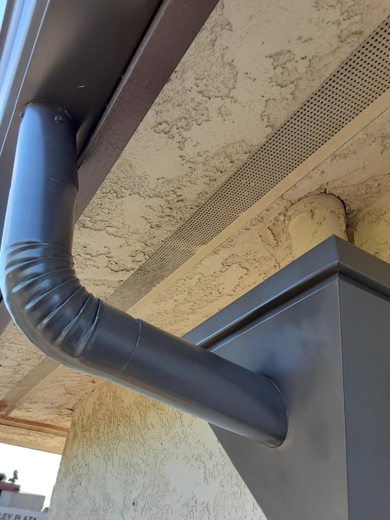 Dark gray gutter pipe extending from roof into a square downspout.