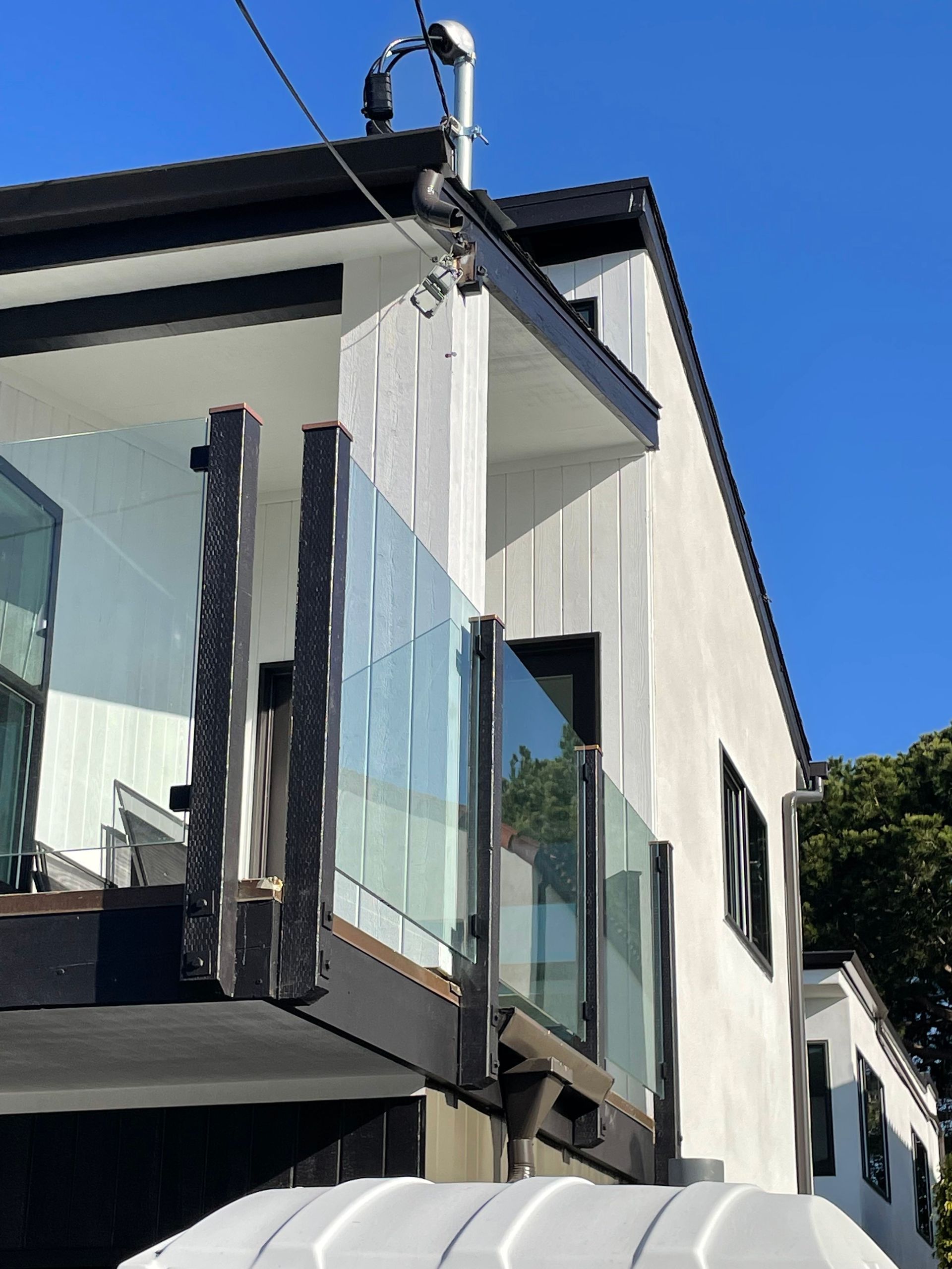 Modern two-story building with black trim and glass balcony against a blue sky.