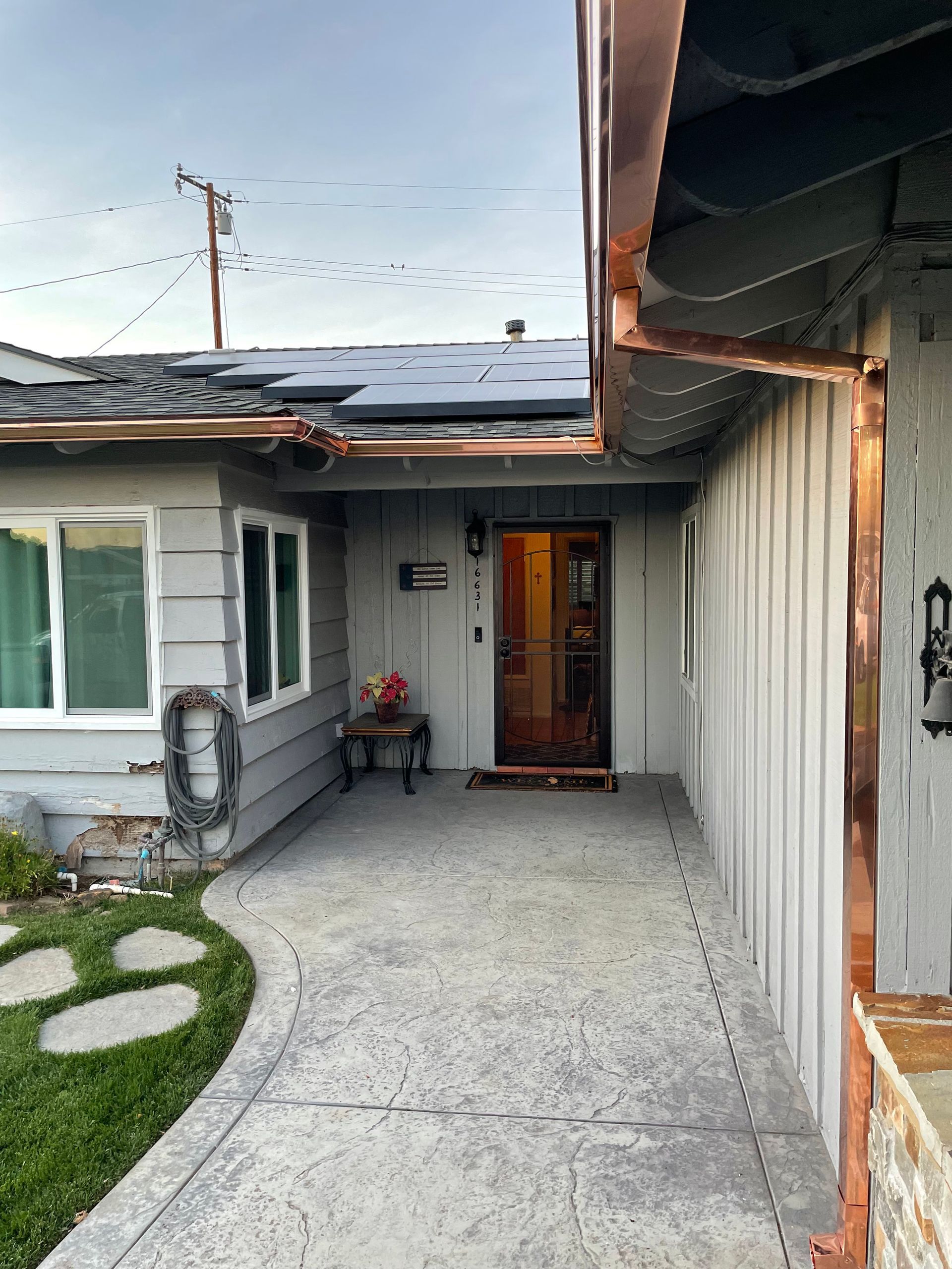 Gray house with copper gutters, concrete walkway, and small porch area.
