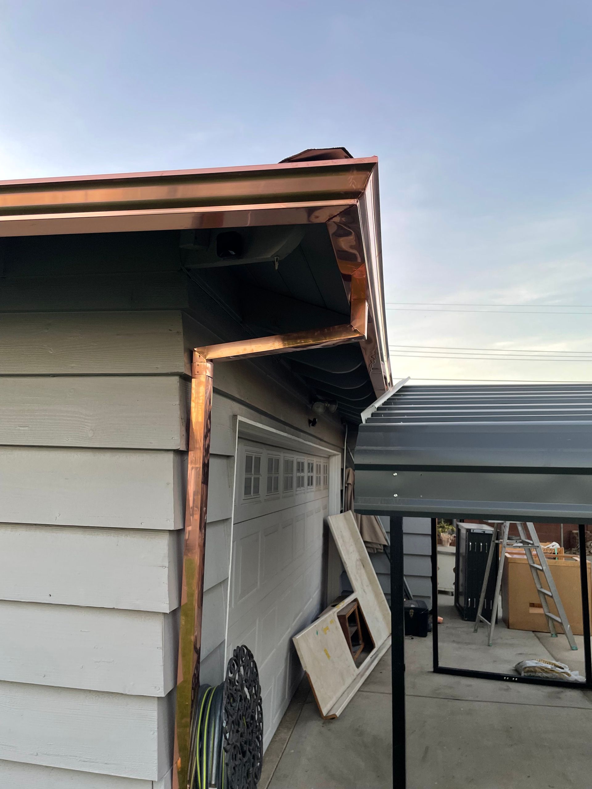 Copper gutters on a house with white siding. A carport is on the right.