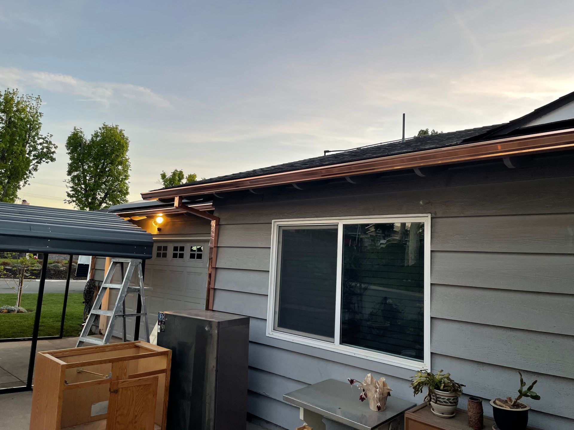 Gray house with copper gutters, window, and nearby boxes and a canopy.