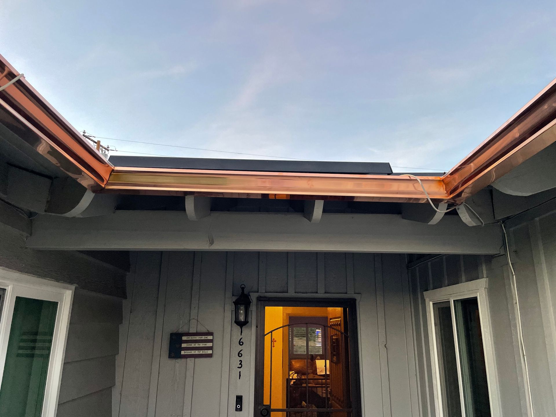 Copper gutters on a grey house above a doorway.