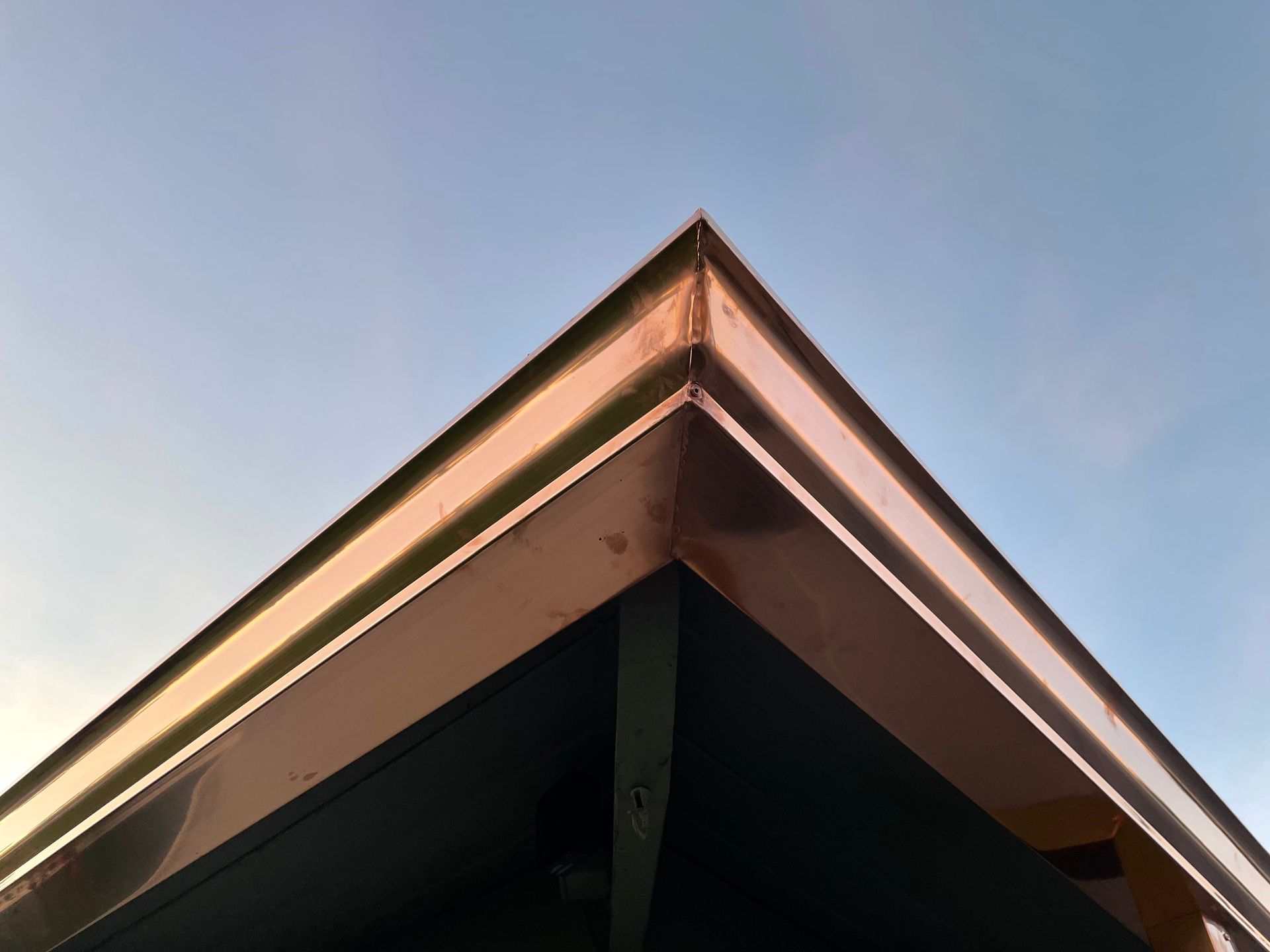Copper-colored roof corner against a blue sky, reflecting sunlight.
