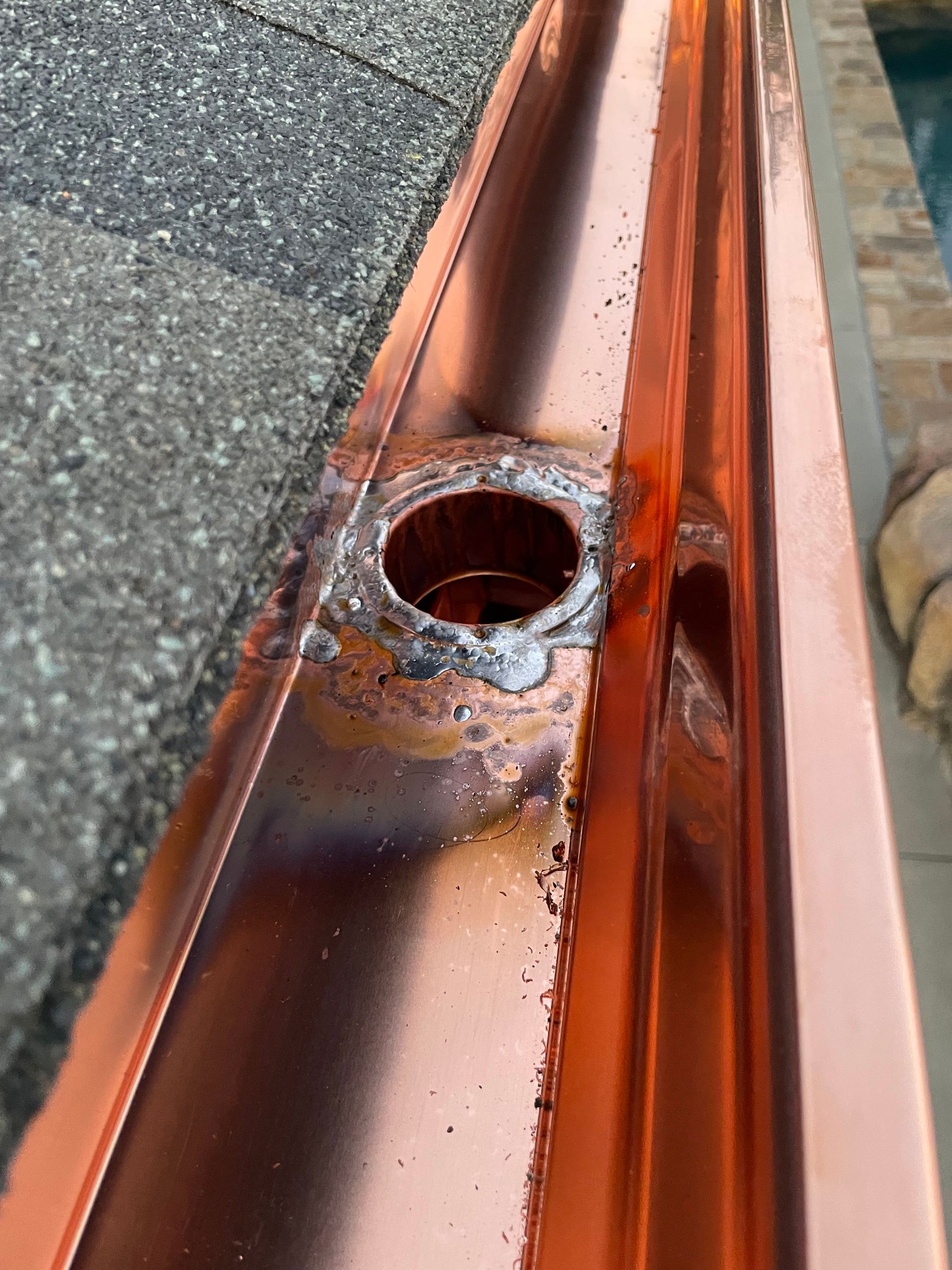 Copper gutter with a welded downspout outlet. The surrounding metal shows signs of heat.