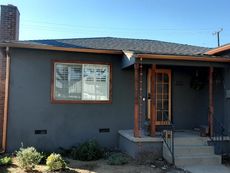Dark gray house with brown trim, a front porch, and a brick chimney under a blue sky.