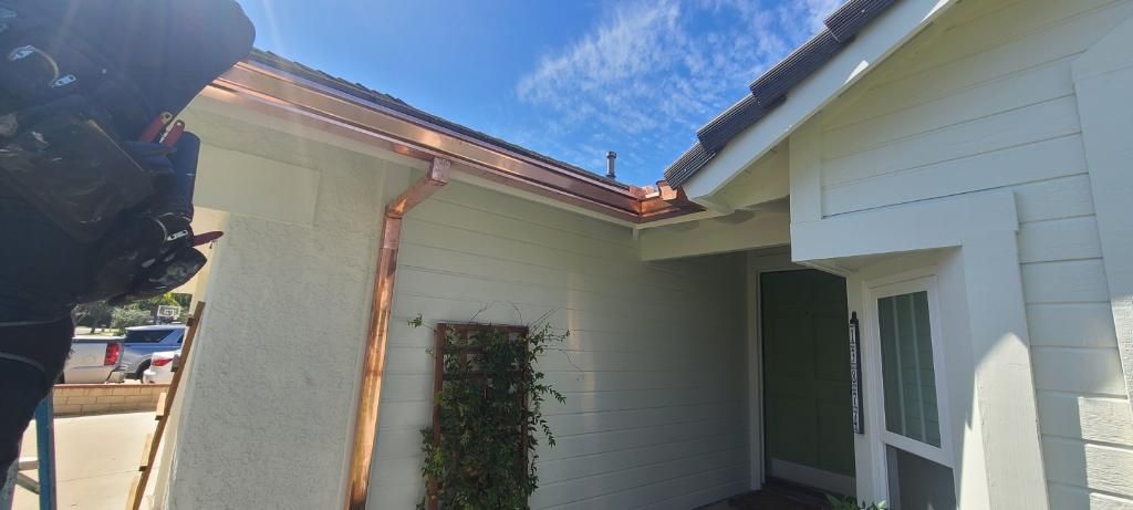 A house with a copper gutter under a blue sky. The house is painted white.