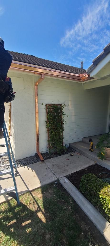 Copper gutters on a house with climbing plants. A person is on a ladder. Blue sky.