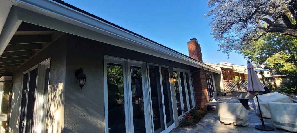 Exterior of a house with multiple glass doors and a brick chimney under a bright blue sky.