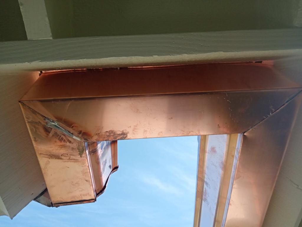 Copper-clad opening in a building's soffit, angled toward a blue sky.
