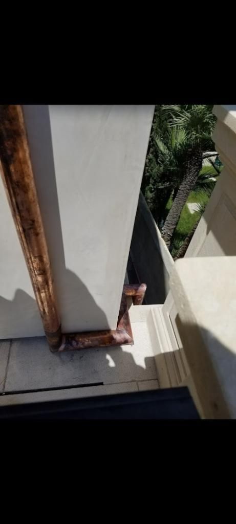 Copper gutter on a stone wall, with green foliage in the background.