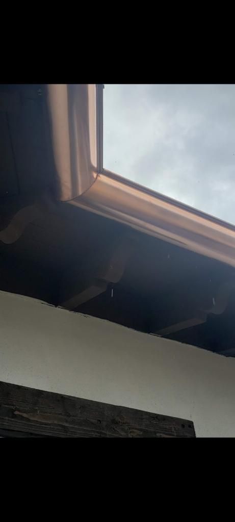 Brown roof gutter against a cloudy sky, a white wall is below.