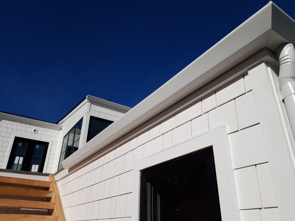 White building with clapboard siding, gutters, and downspout against a blue sky.