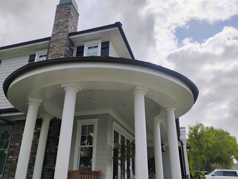 White portico with columns and black trim on a light gray house under a cloudy sky.
