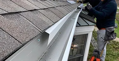 Man cleaning a gutter on a roof. The gray gutter is filled with debris.