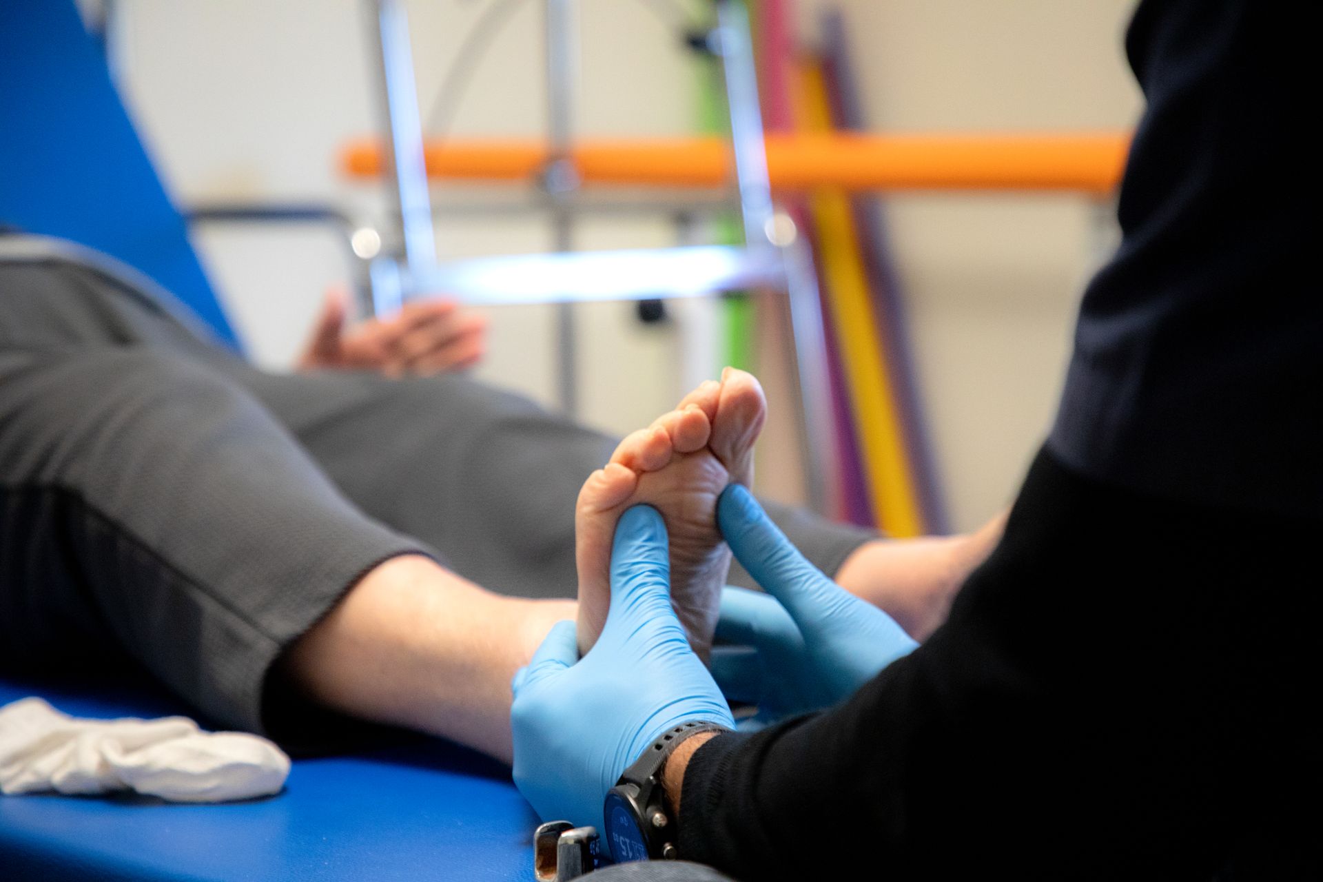 Il piede di una persona viene esaminato da una persona che indossa guanti blu in un ambiente medico.