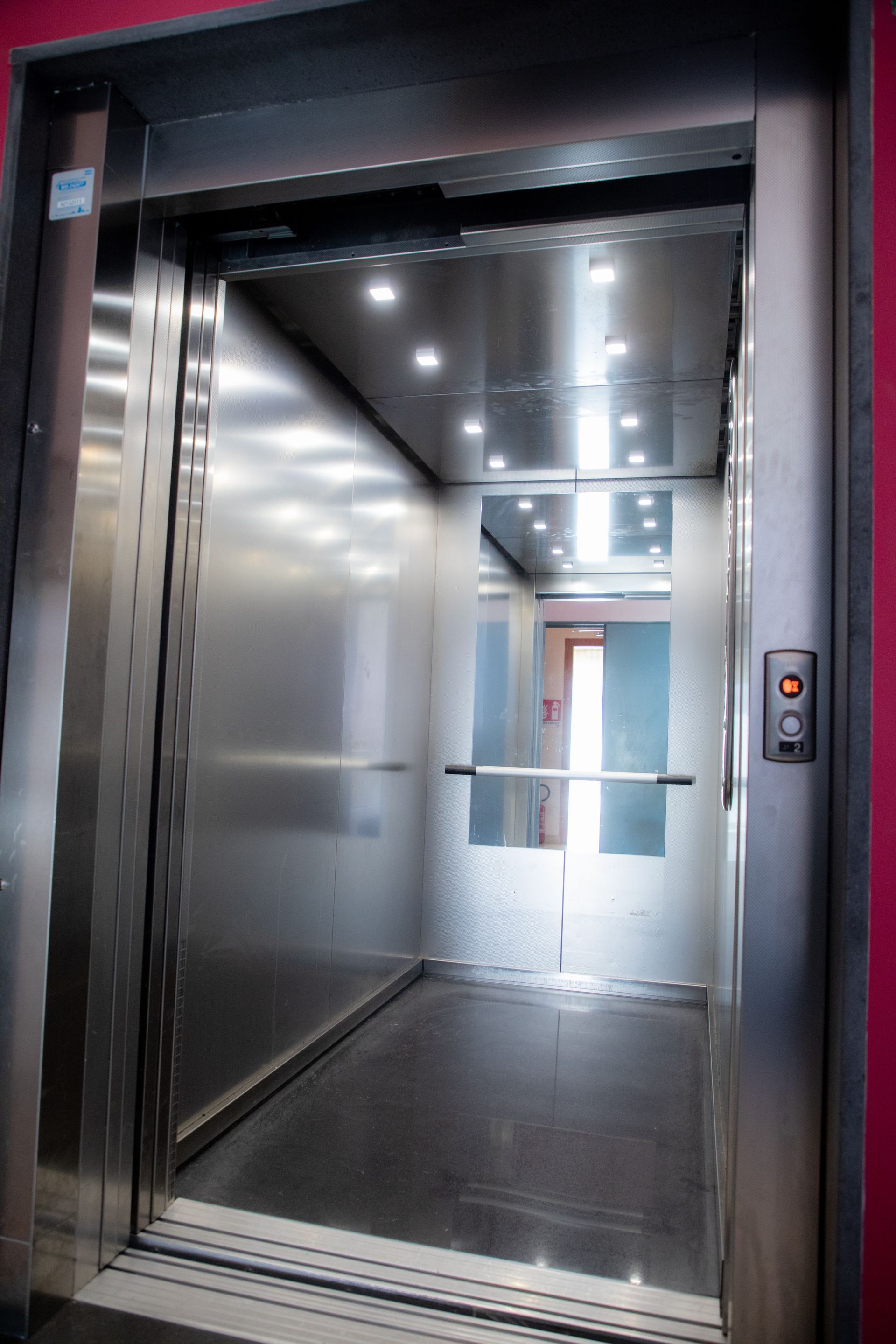 Cabina ascensore aperta, interni in acciaio inox, porta aperta, pulsantiera a destra.